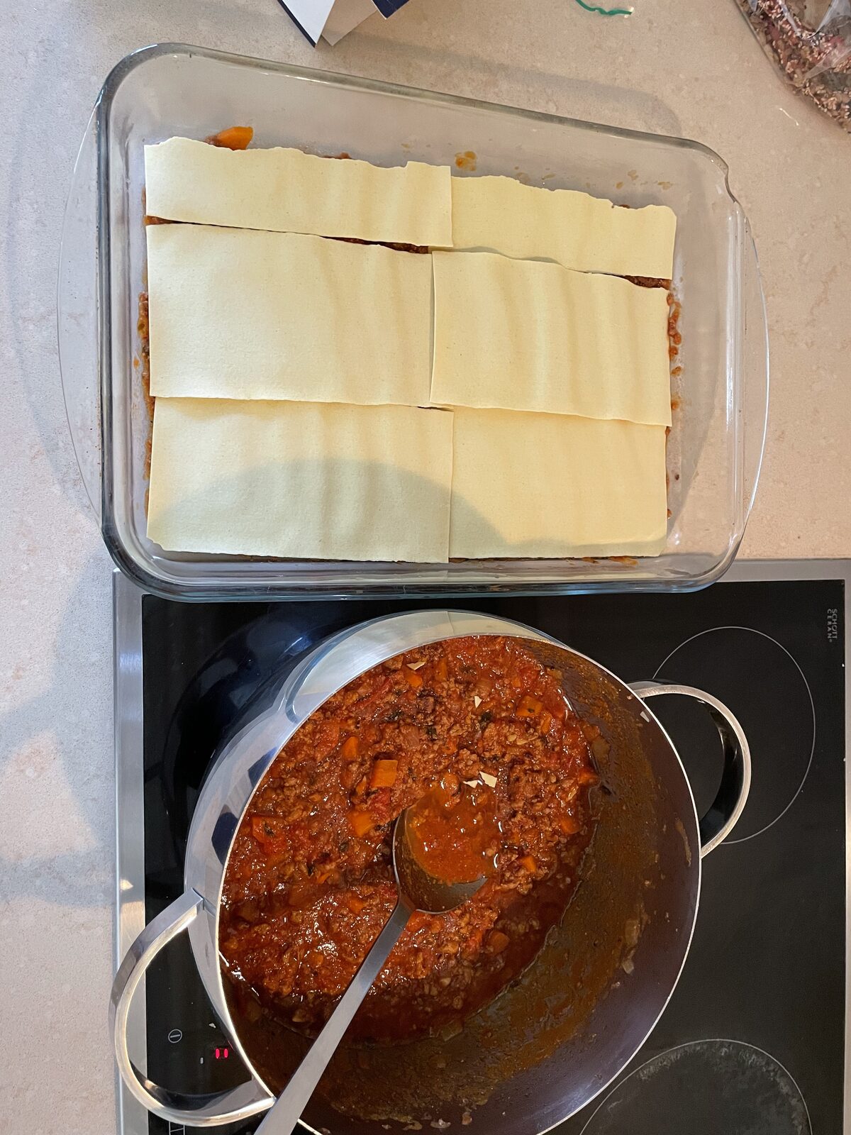 Pasta sheets laid over the ragù, next to the pot of sauce